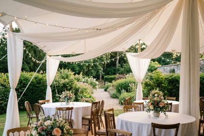 Salle de fête installée dans un jardin avec chapiteau blanc, tables rondes décorées et guirlandes lumineuses pour une célébration en famille